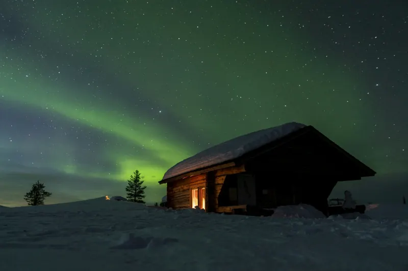 Holzhütte im Schnee unter grünem Nordlicht